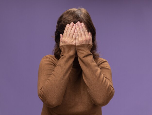 Femme d'âge moyen en col roulé marron face de fermeture avec les bras debout sur le mur violet