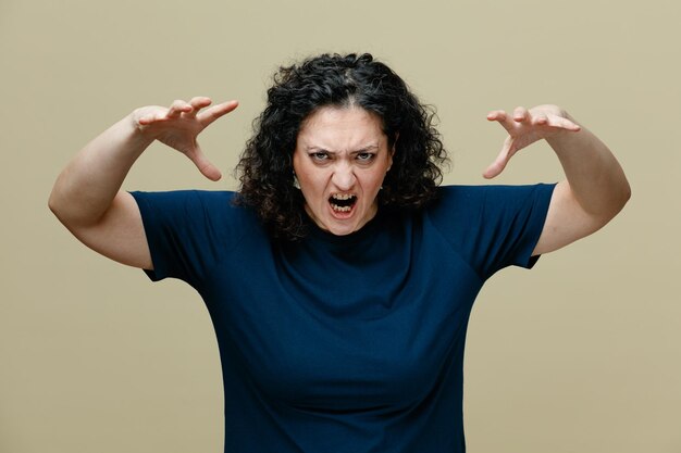 Femme d'âge moyen en colère portant un t-shirt regardant la caméra faisant un rugissement de tigre et un geste de pattes isolé sur fond vert olive