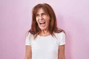 Photo gratuite femme d'âge moyen debout sur fond rose en colère et folle criant frustré et furieux, criant de colère. rage et concept agressif.