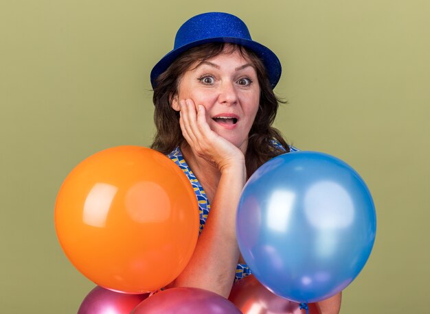 Femme d'âge moyen heureuse et excitée en chapeau de fête avec bouquet de ballons colorés