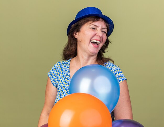Femme d'âge moyen heureuse et excitée en chapeau de fête avec un tas de ballons colorés en riant