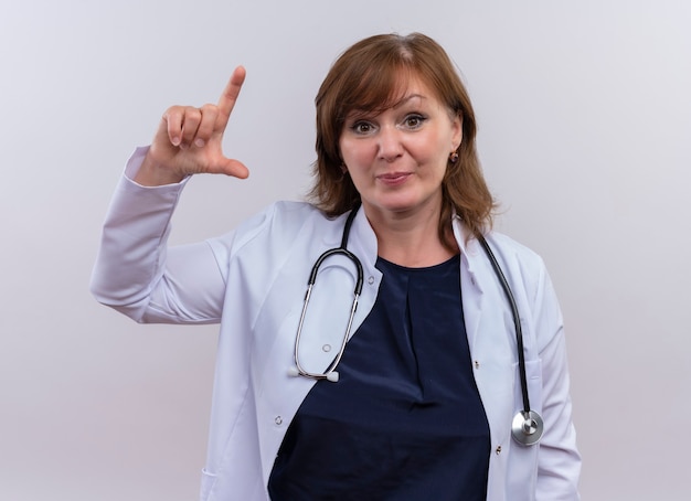 Photo gratuite femme d'âge moyen médecin portant une robe médicale et un stéthoscope faisant un geste de mesure à la recherche sur un mur blanc isolé