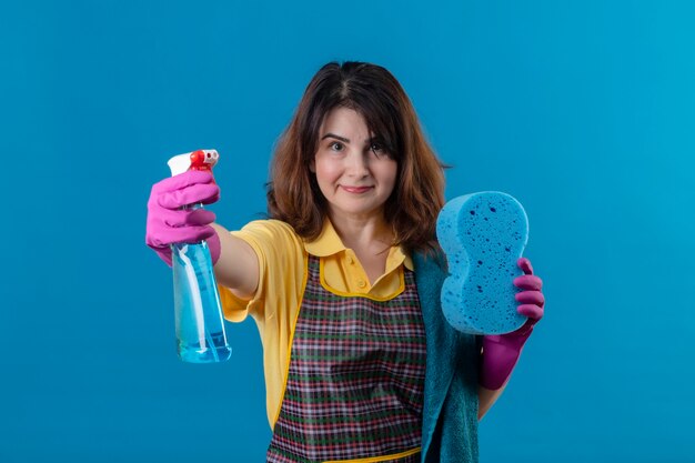 Femme d'âge moyen portant un tablier tenant un spray de nettoyage et une éponge souriant