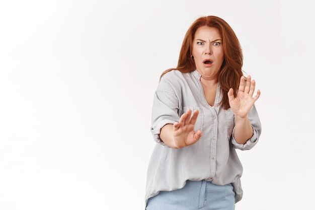 Une femme d'âge moyen rousse mécontente grinçante montre de l'aversion reculer réticents lever les mains défensives grimaçant mécontent terrible odeur terrible, mur blanc