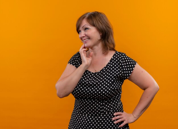 Femme d'âge moyen souriante mettant les mains sur la poitrine et la taille sur un mur orange isolé avec espace copie