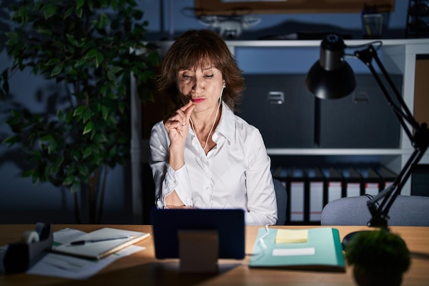 Femme d'âge moyen travaillant au bureau la nuit, la bouche et les lèvres fermées comme une fermeture éclair avec les doigts. secret et silencieux, parler tabou