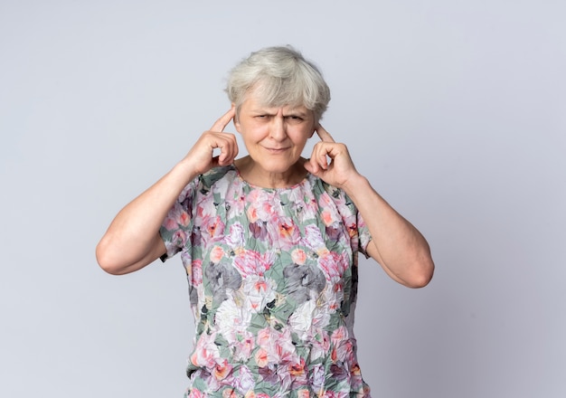 Femme âgée agacée ferme les oreilles avec les doigts isolés sur un mur blanc