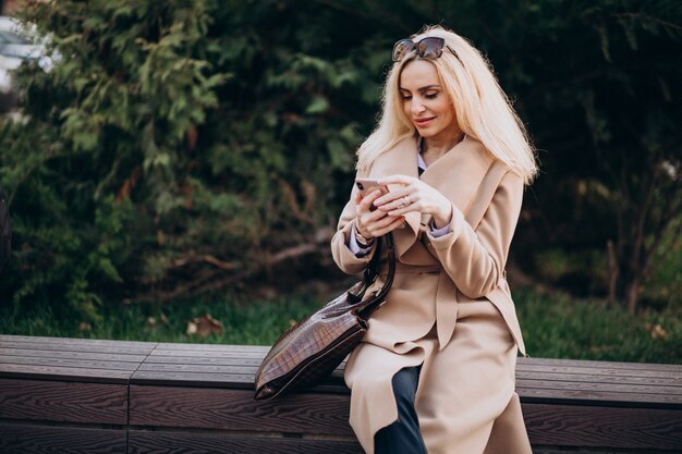 Femme âgée assise sur un banc dans le parc et parler au téléphone