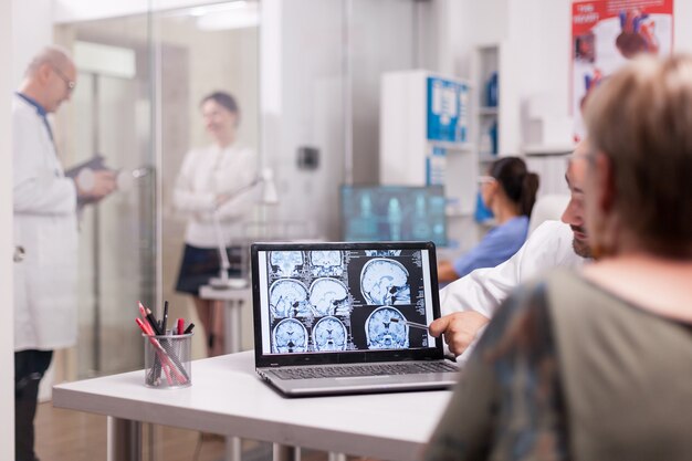 Femme âgée au bureau de l'hôpital regardant un scanner cérébral tout en discutant avec un médecin du diagnostic. Jeune femme malade et infirmier âgé aux cheveux gris dans le couloir de la clinique.