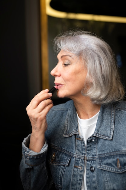 Photo gratuite femme âgée buvant du café dans un café et rafraîchissant son maquillage à l'aide de rouge à lèvres