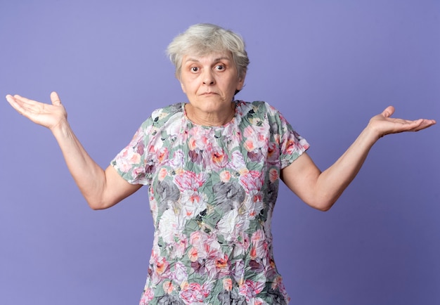 Femme âgée confuse se tient avec les mains ouvertes isolé sur mur violet