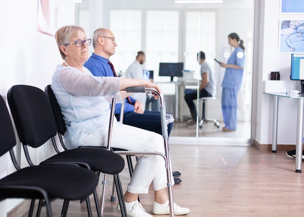 Femme âgée avec déambulateur dans la salle d'attente de l'hôpital pour un traitement de réadaptation