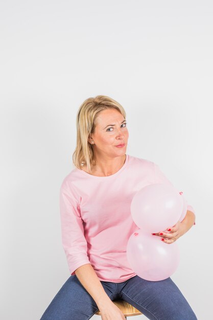 Femme âgée drôle en chemisier rose sur un tabouret avec des ballons