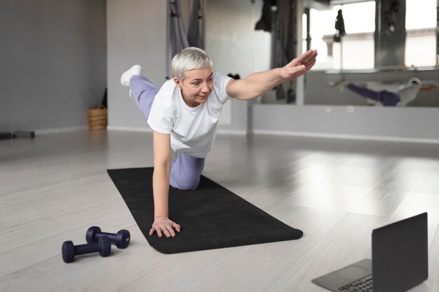 Femme âgée faisant du yoga sur un tapis de yoga dans la salle de sport