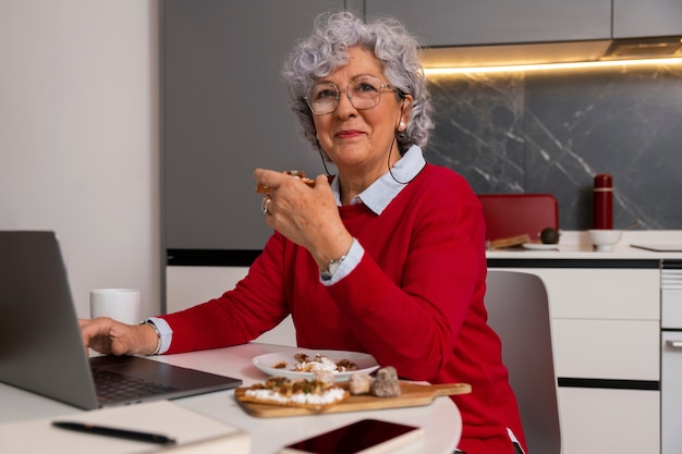 Photo gratuite femme âgée mangeant un plat de figues à la maison et utilisant un ordinateur portable