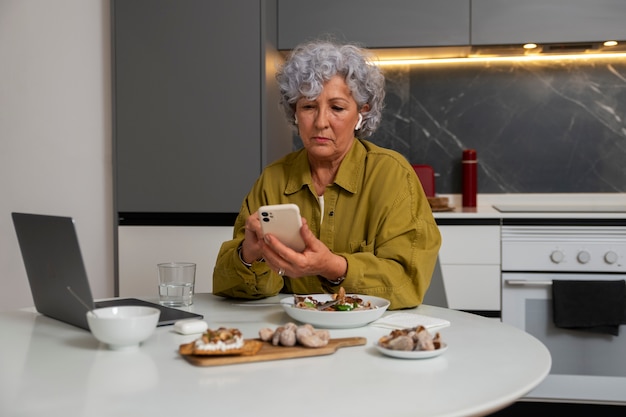 Photo gratuite femme âgée mangeant un plat de figues à la maison et utilisant un smartphone