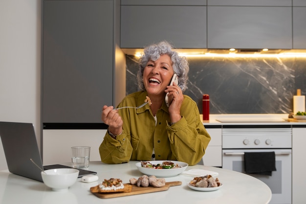 Photo gratuite femme âgée mangeant un plat de figues à la maison et utilisant un smartphone