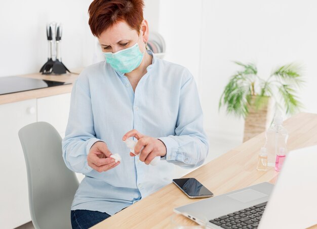 Femme âgée avec un masque médical désinfectant ses appareils