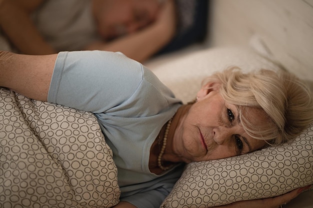 Femme âgée mécontente pensant en position couchée dans son lit éveillée tard dans la nuit