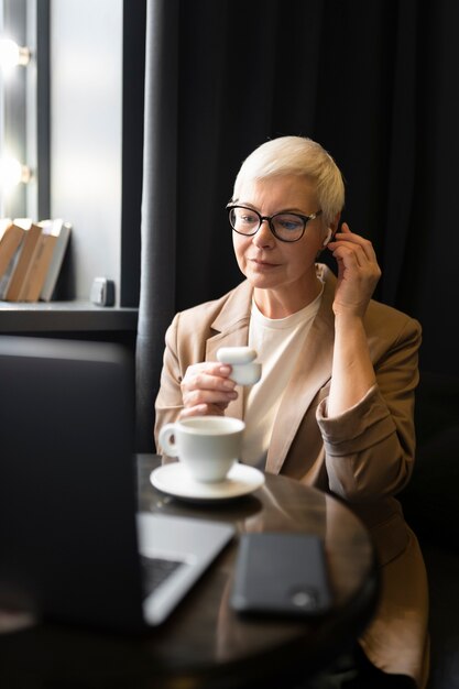 Femme âgée mettant ses écouteurs dans ses oreilles et buvant du café dans un café