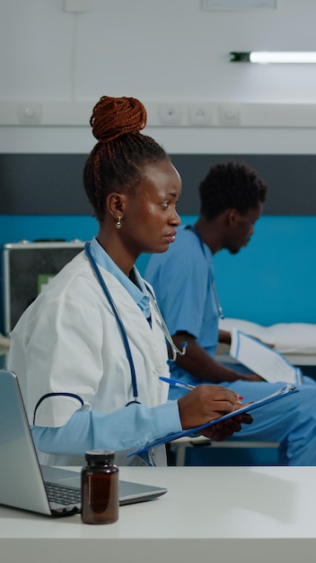 Femme âgée recevant des conseils médicaux d'une infirmière alors qu'elle était assise sur son lit dans une armoire de l'établissement. Jeune médecin parlant à un patient âgé au bureau tout en écrivant des informations de contrôle