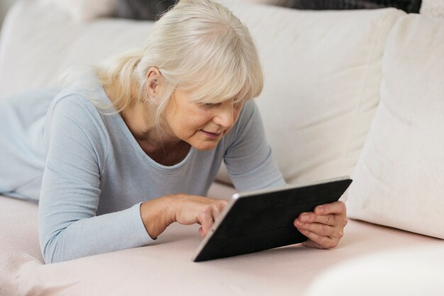 Femme âgée reposant sur le canapé et la tablette de navigation