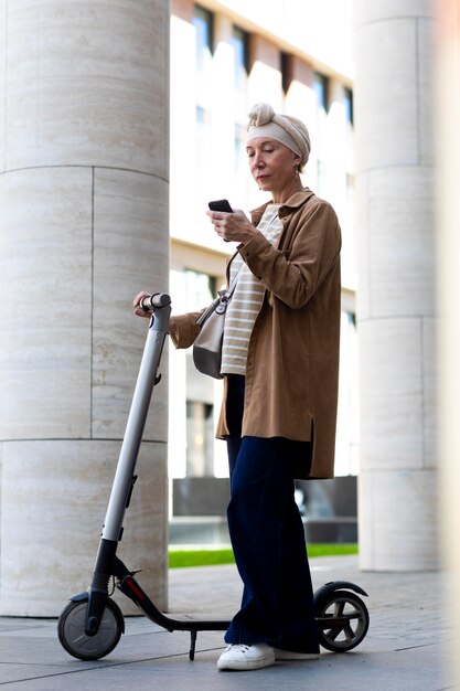 Femme âgée avec un scooter électrique dans la ville à l'aide d'un smartphone