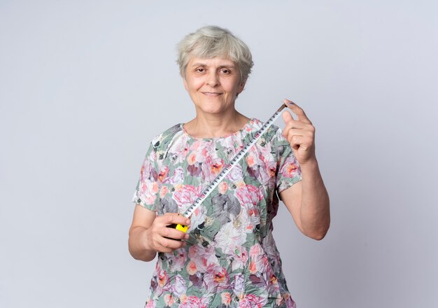 Femme âgée souriante tient un ruban à mesurer isolé sur un mur blanc