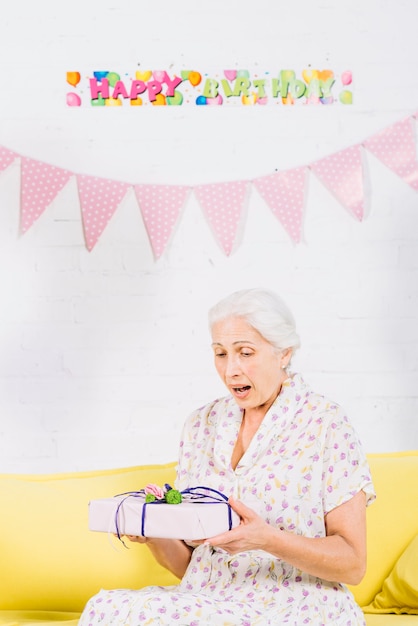 Photo gratuite femme âgée surprise regardant un cadeau d'anniversaire