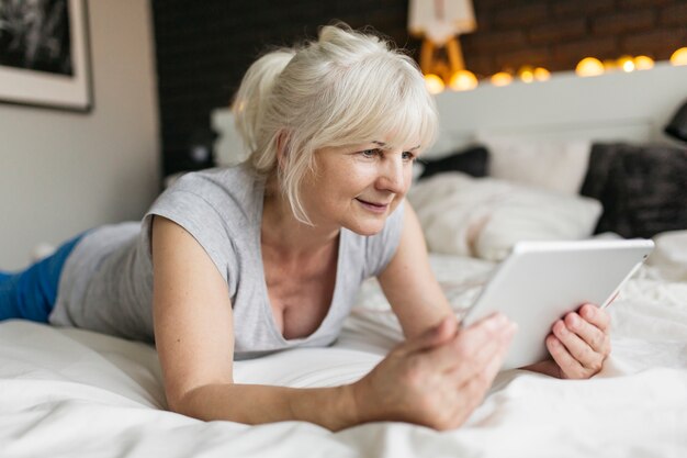 Femme âgée avec tablette sur le lit