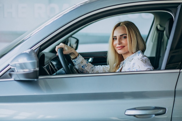 Femme âgée testant une voiture dans une salle d'exposition automobile