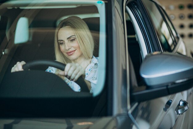 Femme âgée testant une voiture dans une salle d'exposition automobile