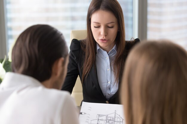 Femme agent immobilier sérieux discute du plan de construction de la maison avec les clients