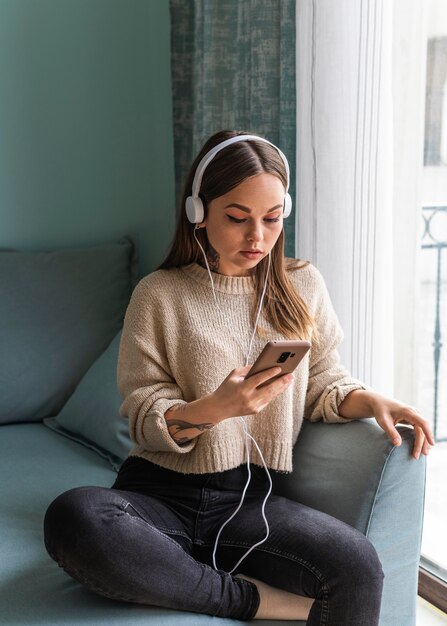 Femme à l'aide d'un casque et d'un smartphone à la maison pendant la pandémie