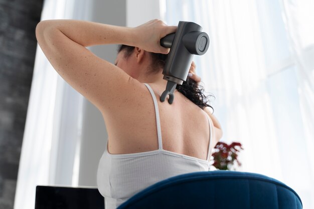 Femme à l'aide d'un pistolet de massage à faible angle