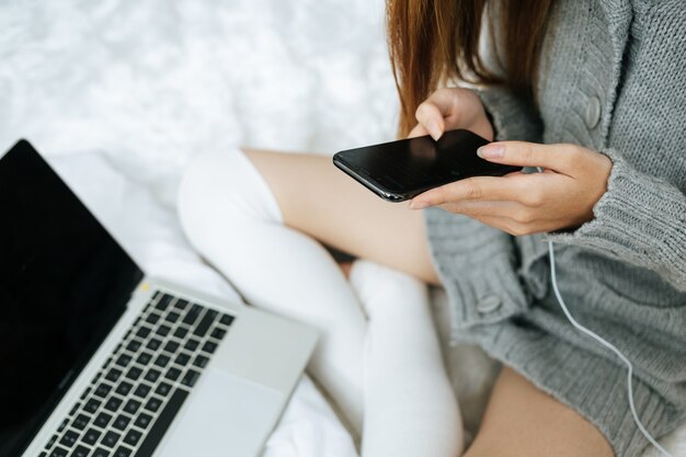 Femme à l'aide de smartphone sur son lit par temps froid