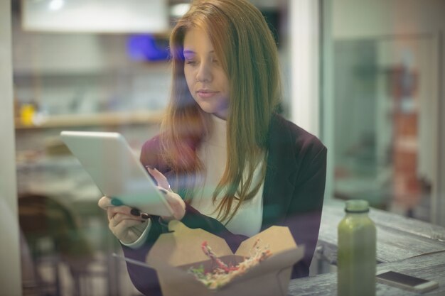 Femme à l'aide de tablette numérique en mangeant de la salade