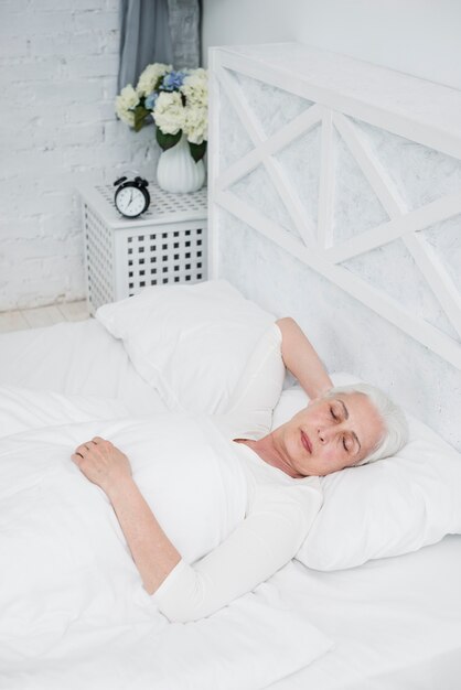 Femme aînée dormant sur un lit blanc