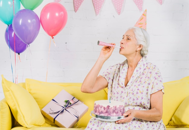 Photo gratuite femme aînée, à, gâteau anniversaire, souffler corne fête