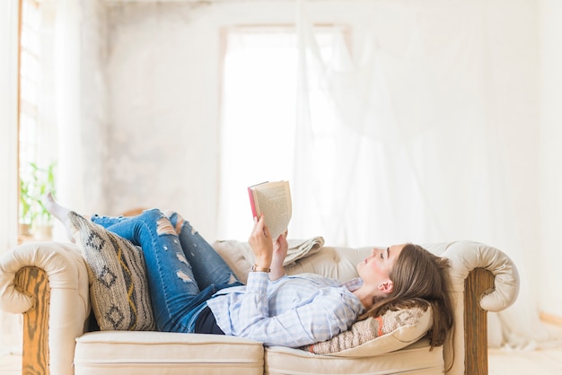 Femme allongée lisant un roman sur un canapé