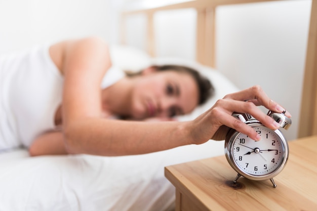 Photo gratuite femme allongée sur le lit en éteignant le réveil dans la chambre