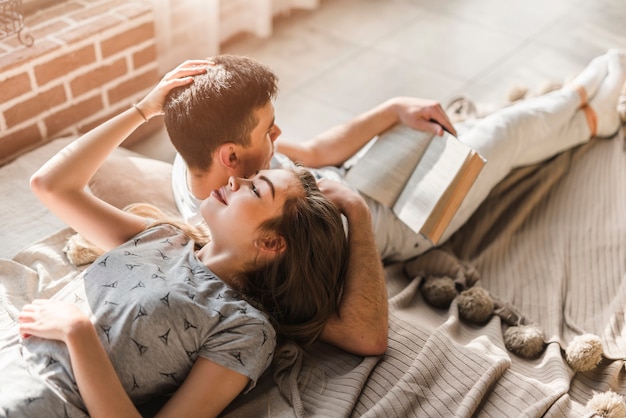 Photo gratuite femme allongée sur un lit et homme lisant un livre à la maison