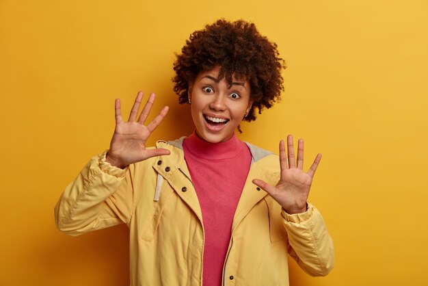 Une femme amusée et ludique avec des cheveux afro montre des paumes à la caméra, joue avec un petit enfant, se trompe et sourit joyeusement, a une humeur optimiste