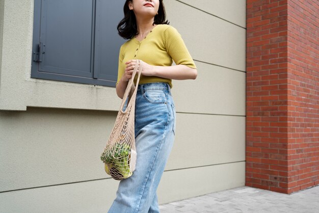 Femme à angle bas portant des provisions dans un sac fourre-tout