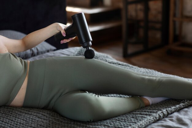 Femme à angle élevé utilisant un pistolet de massage sur la hanche