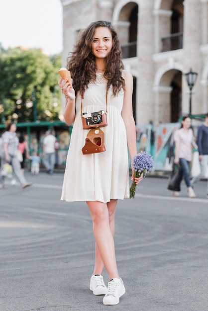 Femme avec appareil photo debout avec crème glacée et fleurs