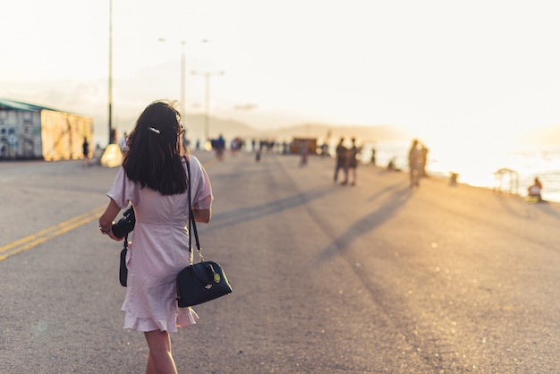 Femme avec un appareil photo marchant près d'une plage par une journée ensoleillée