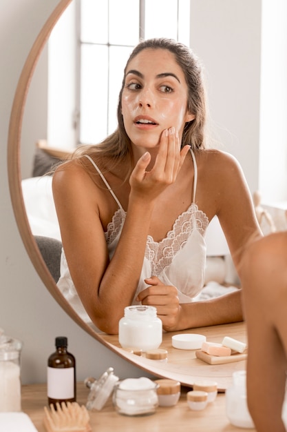 Femme appliquant la crème et regardant dans le miroir
