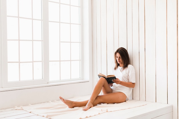 Femme appréciant la lecture sur la couverture près de la fenêtre