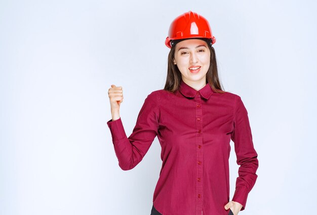 Femme architecte réussie en casque dur rouge debout et lève le pouce.